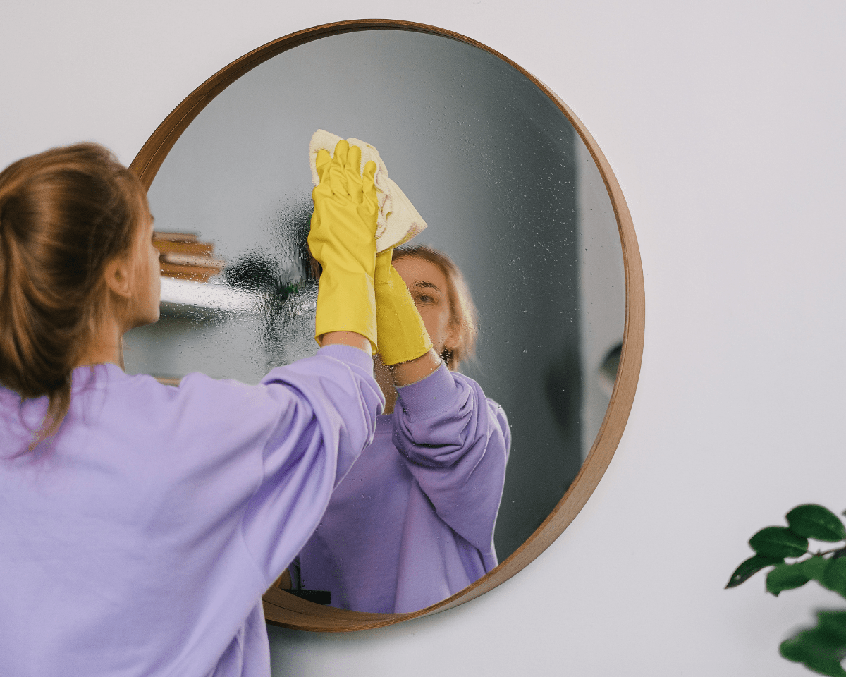 je huis weer eens echt fris en hygiënisch door een voorjaarsschoonmaak, vrouw maakt spiegel schoon met keukenhandschoen en schoonmaakmiddel